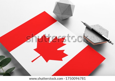 Canada flag on minimalist paper background. National invitation letter with stylish pen on stone. Communication concept.