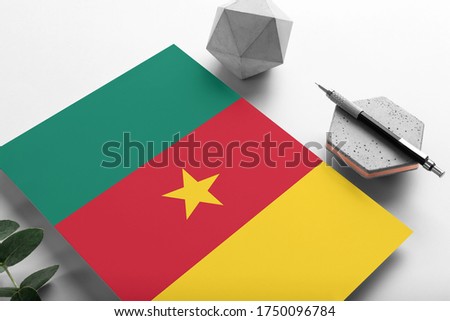 Cameroon flag on minimalist paper background. National invitation letter with stylish pen on stone. Communication concept.