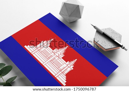 Cambodia flag on minimalist paper background. National invitation letter with stylish pen on stone. Communication concept.