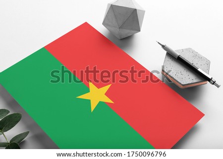 Burkina Faso flag on minimalist paper background. National invitation letter with stylish pen on stone. Communication concept.