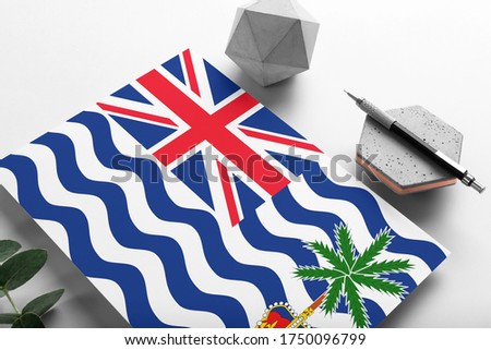 British Indian Ocean Territory flag on minimalist paper background. National invitation letter with stylish pen on stone. Communication concept.