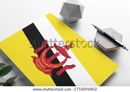 Brunei flag on minimalist paper background. National invitation letter with stylish pen on stone. Communication concept.