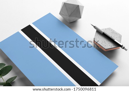 Botswana flag on minimalist paper background. National invitation letter with stylish pen on stone. Communication concept.