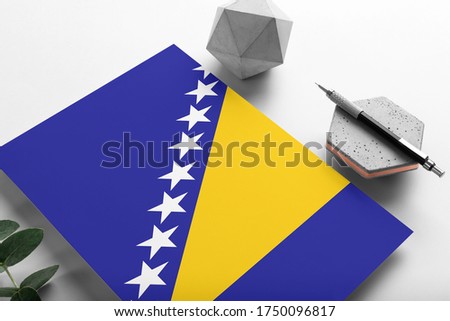 Bosnia Herzegovina flag on minimalist paper background. National invitation letter with stylish pen on stone. Communication concept.