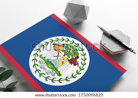 Belize flag on minimalist paper background. National invitation letter with stylish pen on stone. Communication concept.