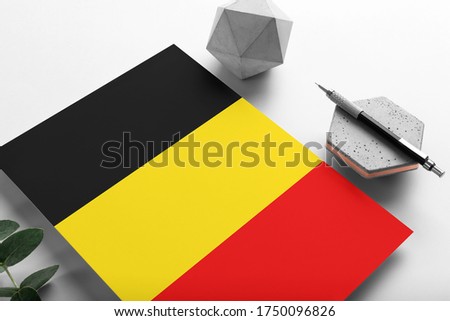 Belgium flag on minimalist paper background. National invitation letter with stylish pen on stone. Communication concept.