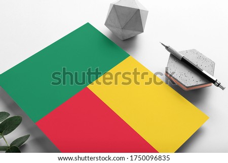Benin flag on minimalist paper background. National invitation letter with stylish pen on stone. Communication concept.
