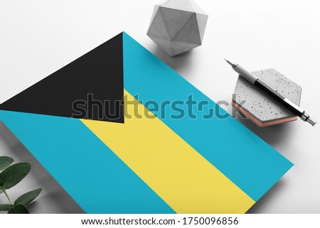 Bahamas flag on minimalist paper background. National invitation letter with stylish pen on stone. Communication concept.