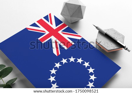 Cook Islands flag on minimalist paper background. National invitation letter with stylish pen on stone. Communication concept.