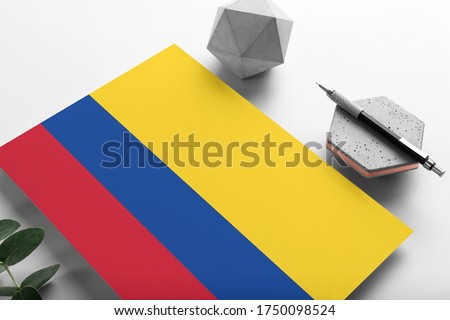 Colombia flag on minimalist paper background. National invitation letter with stylish pen on stone. Communication concept.