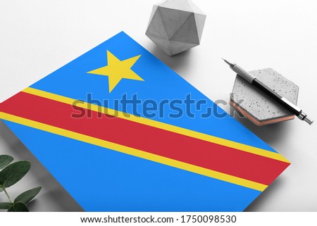 Congo flag on minimalist paper background. National invitation letter with stylish pen on stone. Communication concept.