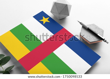 Central African Republic flag on minimalist paper background. National invitation letter with stylish pen on stone. Communication concept.