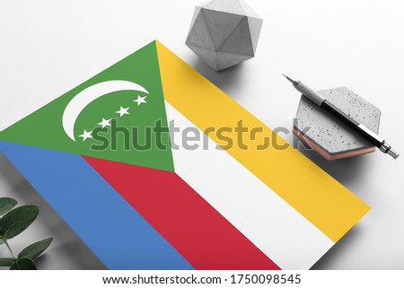 Comoros flag on minimalist paper background. National invitation letter with stylish pen on stone. Communication concept.