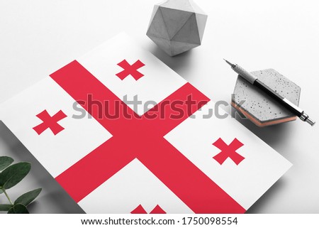 Georgia flag on minimalist paper background. National invitation letter with stylish pen on stone. Communication concept.