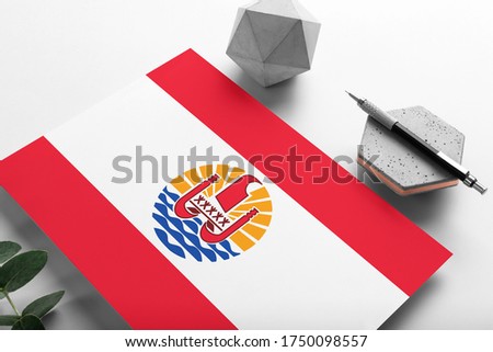 French Polynesia flag on minimalist paper background. National invitation letter with stylish pen on stone. Communication concept.