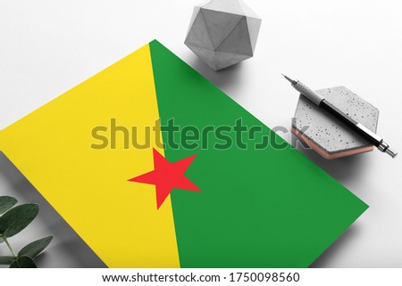French Guiana flag on minimalist paper background. National invitation letter with stylish pen on stone. Communication concept.