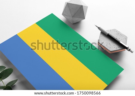 Gabon flag on minimalist paper background. National invitation letter with stylish pen on stone. Communication concept.