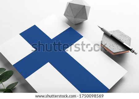 Finland flag on minimalist paper background. National invitation letter with stylish pen on stone. Communication concept.