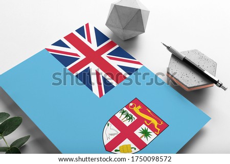 Fiji flag on minimalist paper background. National invitation letter with stylish pen on stone. Communication concept.