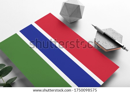 Gambia flag on minimalist paper background. National invitation letter with stylish pen on stone. Communication concept.