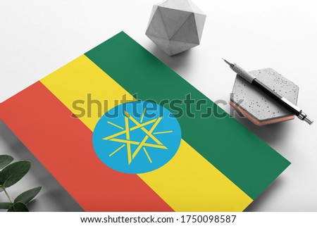 Ethiopia flag on minimalist paper background. National invitation letter with stylish pen on stone. Communication concept.
