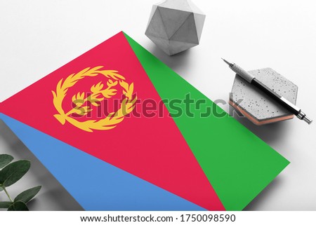 Eritrea flag on minimalist paper background. National invitation letter with stylish pen on stone. Communication concept.