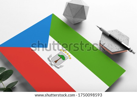 Equatorial Guinea flag on minimalist paper background. National invitation letter with stylish pen on stone. Communication concept.