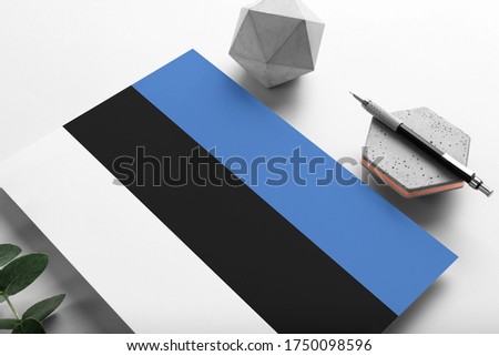 Estonia flag on minimalist paper background. National invitation letter with stylish pen on stone. Communication concept.