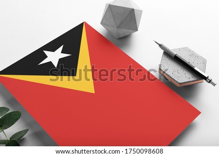 East Timor flag on minimalist paper background. National invitation letter with stylish pen on stone. Communication concept.