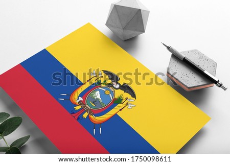 Ecuador flag on minimalist paper background. National invitation letter with stylish pen on stone. Communication concept.