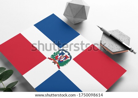 Dominican Republic flag on minimalist paper background. National invitation letter with stylish pen on stone. Communication concept.