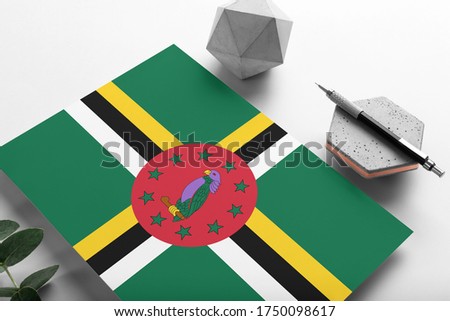 Dominica flag on minimalist paper background. National invitation letter with stylish pen on stone. Communication concept.