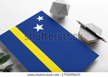 Curacao flag on minimalist paper background. National invitation letter with stylish pen on stone. Communication concept.