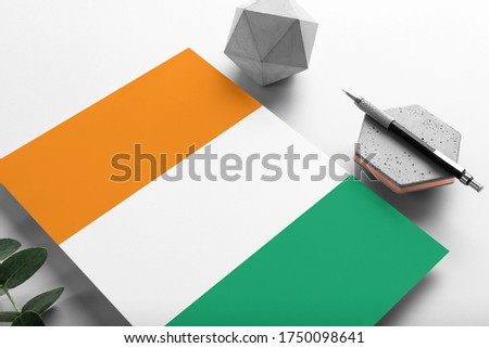 Cote D'Ivoire flag on minimalist paper background. National invitation letter with stylish pen on stone. Communication concept.