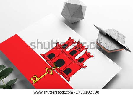 Gibraltar flag on minimalist paper background. National invitation letter with stylish pen on stone. Communication concept.
