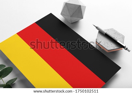Germany flag on minimalist paper background. National invitation letter with stylish pen on stone. Communication concept.