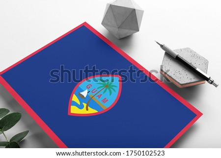 Guam flag on minimalist paper background. National invitation letter with stylish pen on stone. Communication concept.