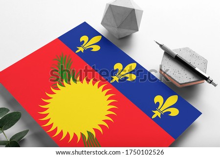 Guadeloupe flag on minimalist paper background. National invitation letter with stylish pen on stone. Communication concept.