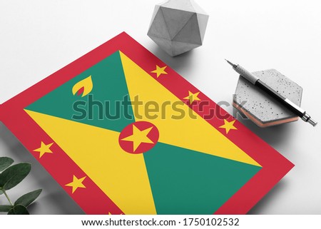 Grenada flag on minimalist paper background. National invitation letter with stylish pen on stone. Communication concept.