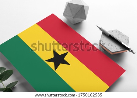Ghana flag on minimalist paper background. National invitation letter with stylish pen on stone. Communication concept.