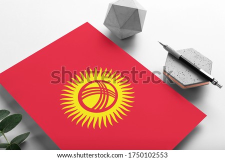 Kyrgyzstan flag on minimalist paper background. National invitation letter with stylish pen on stone. Communication concept.