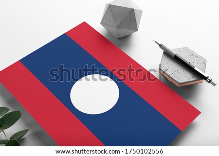 Laos flag on minimalist paper background. National invitation letter with stylish pen on stone. Communication concept.