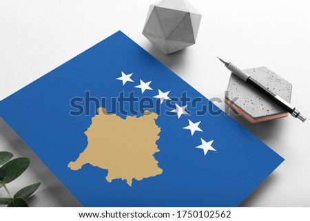 Kosovo flag on minimalist paper background. National invitation letter with stylish pen on stone. Communication concept.