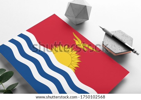 Kiribati flag on minimalist paper background. National invitation letter with stylish pen on stone. Communication concept.