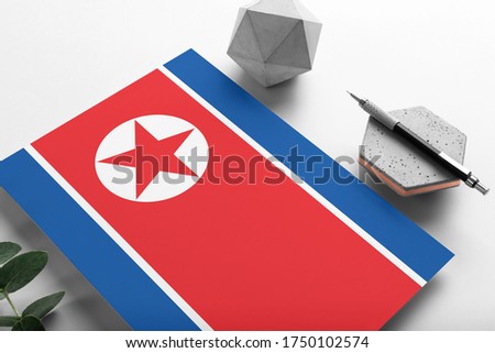 North Korea flag on minimalist paper background. National invitation letter with stylish pen on stone. Communication concept.