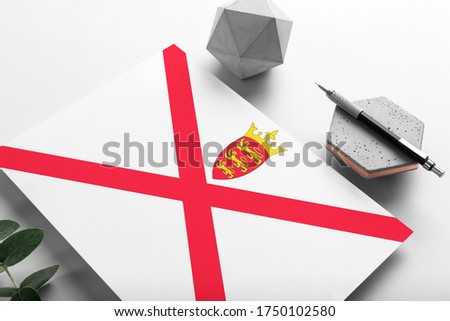 Jersey flag on minimalist paper background. National invitation letter with stylish pen on stone. Communication concept.
