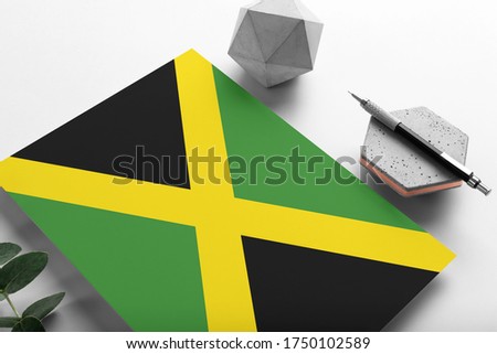 Jamaica flag on minimalist paper background. National invitation letter with stylish pen on stone. Communication concept.