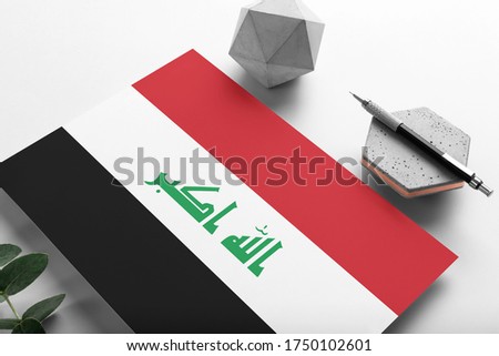 Iraq flag on minimalist paper background. National invitation letter with stylish pen on stone. Communication concept.