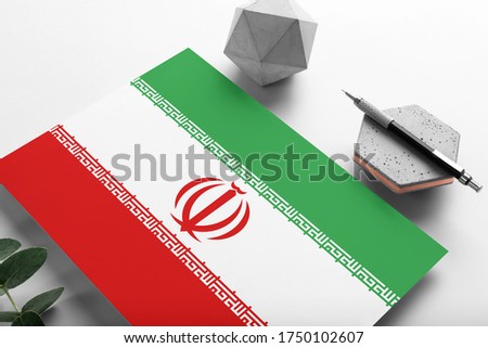 Iran flag on minimalist paper background. National invitation letter with stylish pen on stone. Communication concept.