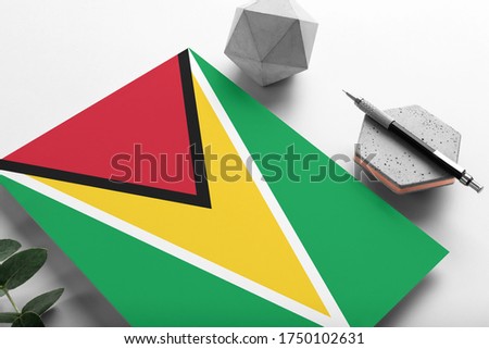 Guyana flag on minimalist paper background. National invitation letter with stylish pen on stone. Communication concept.